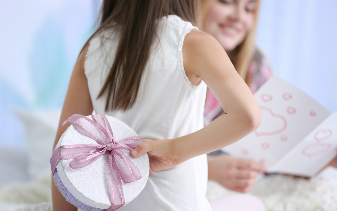 Young girl holds gift behind her back for mom